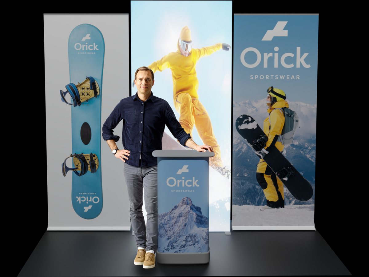 Drei Roll-Ups einer Sportmarke als Rückwand, davor ein Mann an einer kleinen Theke